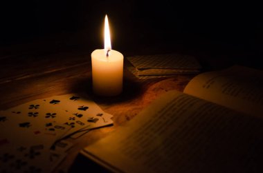Gizemli bir atmosfer, kartlar, bir kitap, tahtadan bir masanın üzerindeki karanlıkta yanan bir mum. Esrarengiz kavram, falcılık ve tahminler