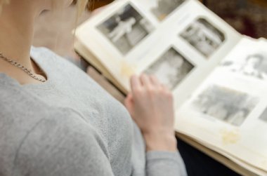 Gri tişörtlü kız kanepede oturuyor ve bir fotoğraf albümündeki eski siyah beyaz fotoğraflara bakıyor.