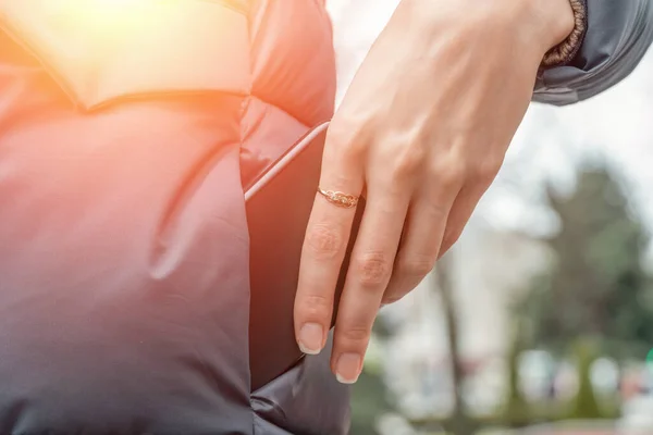 woman\'s hand with a ring pulls a black smartphone out of the pocket of a gray jacket close up. photo with illumination