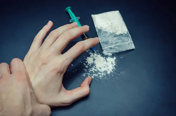 Hand grabs the hand of a drug addict with a package of drugs, a syringe on a black background close-up. You can stop drug addiction by rehabilitation in a rehabilitation center.