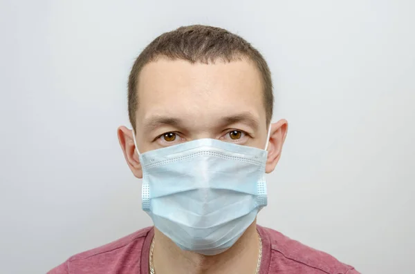 Dark-haired man in a medical mask close-up on a light background