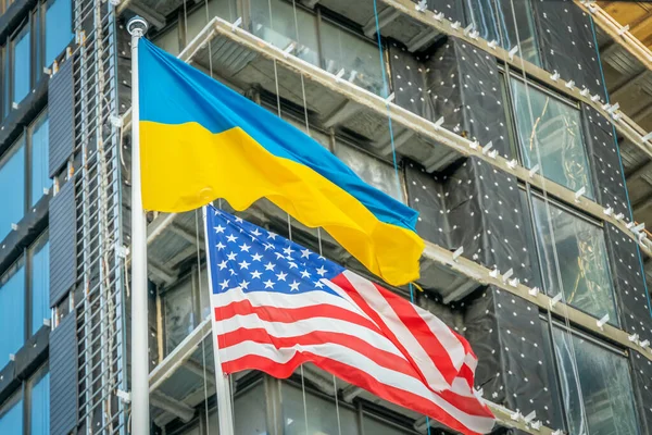 American and Ukrainian flags fly against the blue sky and part of the building. Patriotism.