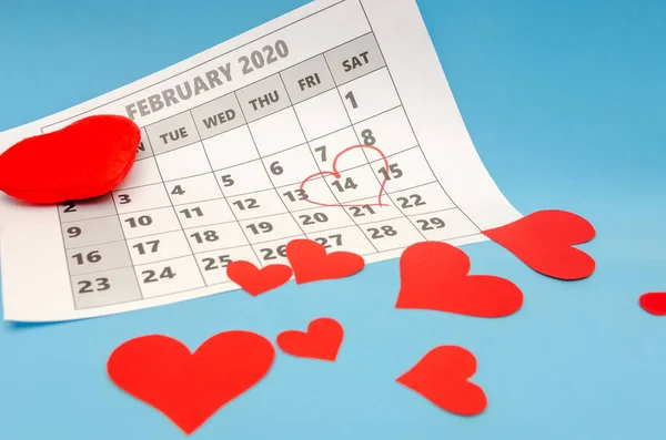 Valentine\'s day 14 is marked with a heart on the calendar, paper hearts are scattered around. Holiday concept
