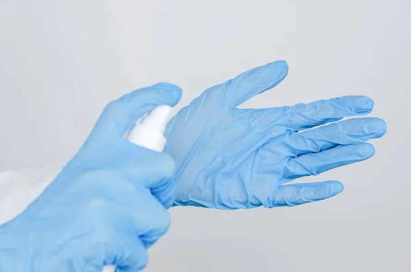 doctor in a white coat and blue gloves disinfects his hands with an antiseptic spray close up