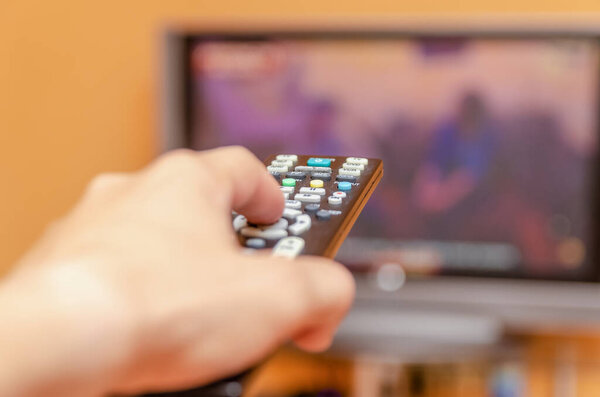 Man's hand holding a tv remote control, pressing a button while pointing at a flat screen tv.