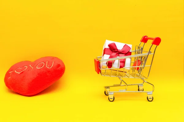 赤いハートの隣の黄色い背景のショッピングカートのギフトボックス スペースをコピーします 贈り物の概念 バレンタインデー — ストック写真