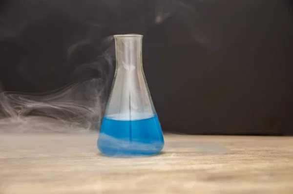 flask with blue liquid in smoke over black background. chemical analysis