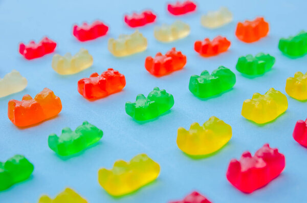 Delicious bright colored jelly bears on a blue background laid out in the same order, side view