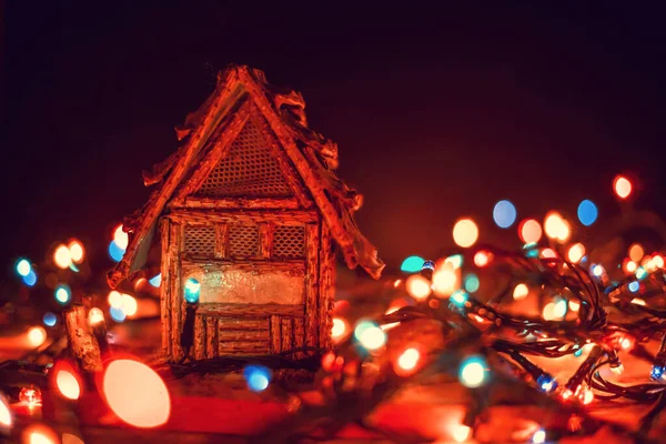 漂亮迷人的圣诞背景贺卡小房子坐落在一个木制的背景上 在圣诞灯的旁边 背景是一个黑色的背景 有一个复制的空间 — 图库照片