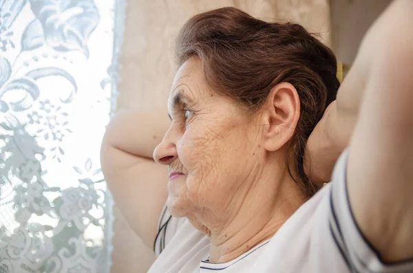 Yaşlı Siyah Saçlı Elleri Başının Arkasında Olan Kadın Pencereden Dışarı — Stok fotoğraf
