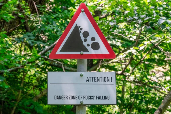 Close-up of a sign of possible rockfall from the mountains against the background of tree branches, warning of danger