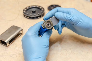 Mavi eldivenli bir erkek, ahşap bir masada elektronik bir sigarayı tamir ediyor.