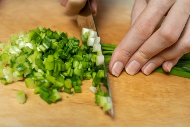 Kadınların elleri, tahta bir tahtada yeşil soğanları bıçakla kesiyor.