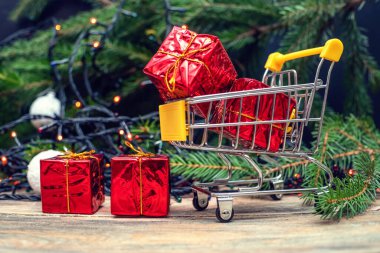 Güzel bir Noel geçmişi. Noel ve Yeni Yıl için hediye konsepti - küçük kırmızı hediyeli alışveriş arabası toplarla Noel ağacının arka planında yakın plan