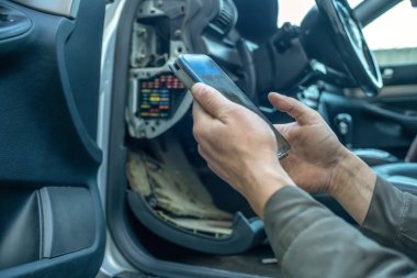 Erkek tamirci arabanın yanında oturan arabanın neden bozulduğuna dair telefon bilgilerine bakıyor. Araba tamiri kavramı