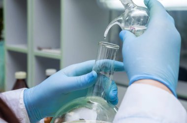 Bir kimyager elinde cam bir test tüpü tutar, sıvı çözeltiyi taşır, kimyasal üretimi kullanarak çeşitli reaktör seçeneklerini kullanarak analiz reaksiyonu yapar. yakın plan