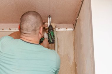 Bir adam elinde matkap tutuyor. Tavanda bir delik aç. Apartmanda tamirat var. İçerideki restorasyon.