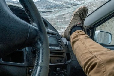 Ayağını arabanın ön camının arka planındaki gösterge paneline koy. Kazadan sonra ön cam kırılmış.