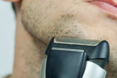 Adam elektrikli jiletle tıraş oluyor.