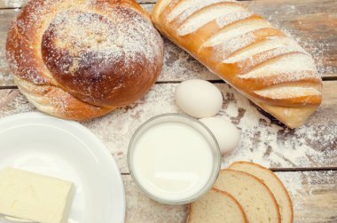 Bir bardak süt, bir somun ekmek, iki yumurta, ahşap zemin üzerinde un ile tereyağı. Kahvaltı konsepti