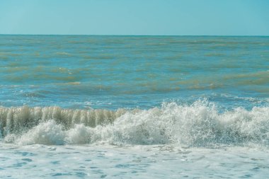 Güneşli bir günde, beyaz köpüklü deniz dalgası kıyıya vurur. Güneşli bir günde Karadeniz kıyısında dalgalar