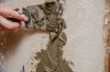 Duvarda içinde elektrik kabloları olan teknik bir delik. Spatula ve çimento karışımlı usta deliği kapatıyor, güvenlik.