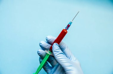 Mavi eldivenler, üzerinde kan ya da aşı bulunan bir şırıngayı mavi bir arka planda tutuyor.