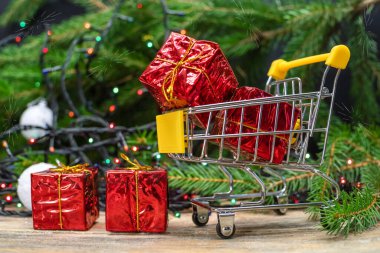 Güzel bir Noel geçmişi. Noel ve Yeni Yıl için hediye konsepti - küçük kırmızı hediyeli alışveriş arabası toplarla Noel ağacının arka planında yakın plan