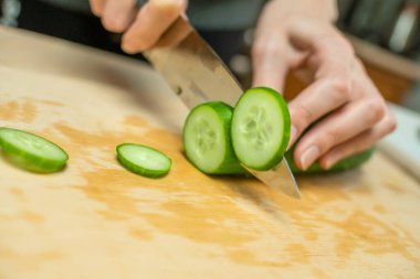 Kadınların elleri taze bir salatalığı ahşap bir tahtanın üzerinde daire şeklinde kesiyor.