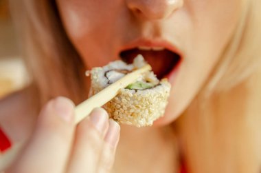 Susamlı suşi yiyen güzel sarışın kadın. Sığ alan derinliği, suşiye odaklan. Güzel ağız ve suşi planı.