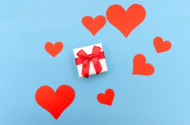 Mavi arka planda kırmızı kağıt kalpler arasında bir hediye kutusu. Üst görünüm, boşluğu kopyala. Sevgililer Günü, aşkın sembolü. Neşeli arkaplan