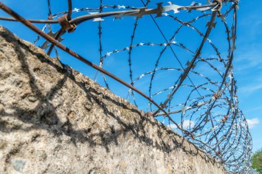 Mavi gökyüzüne karşı çitin etrafına sarılmış dikenli teller.