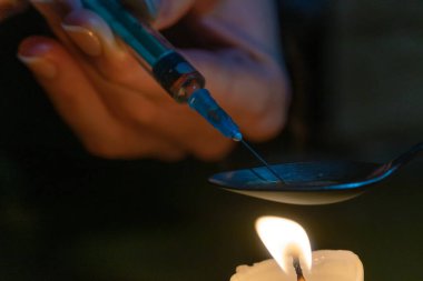 Mumun üzerinde uyuşturucuyu eritmek. İğne ve şırınga, kaynayan ilacı kaşıktan çıkarır. Mumun üzerinde şırıngası olan bir uyuşturucu bağımlısının elleri.