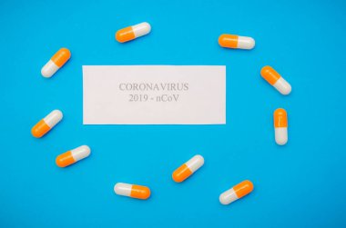 Mavi arka planda turuncu ve beyaz kapsüller arasında Coronavirus yazısıyla beyaz bir sayfa. Tıbbi arka plan, üst görünüm