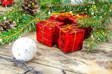 Noel ağacı dalları ve Noel baloları arasında tahta bir arka planda kırmızı mini hediyeler. Güzel Noel arkaplanı