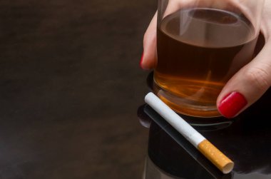Bir bardak viskiyi sigarayla tutan bir kız.
