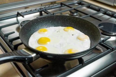Altı yumurta yakın planda, tavada, gaz ocağında kızarıyor.