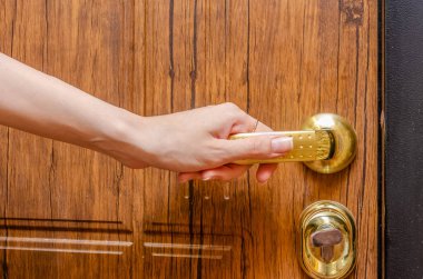 Ahşap bir kapının altın sapını tutan kadın eli. Yaklaş.