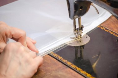 Eski bir dikiş makinesine dikiş diken bir kadının elleri.