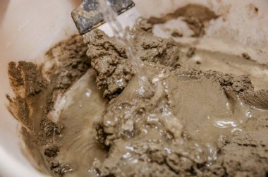Çimentoyla suyu birbirine karıştırıyorum. Bir spatulayla çimento ve su karışımı.