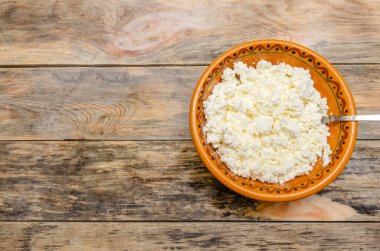 Ahşap arka planda kahverengi bir kasede süzme peynir. Sağlıklı Kahvaltı, üst görünüm, boşluğu kopyala