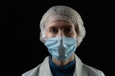 Tıbbi maskeli genç bayan doktor, siyah arkaplan ve önlüklü fotokopi alanı olan