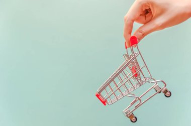Kadının eli mavi arka planda bir alışveriş arabasını tutuyor. Boşluğu kopyala
