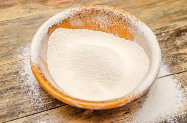 Seramik kahverengi bir kasede un ve ahşap arka planda serpiştirilmiş un. Yukarıdan görünüşü