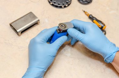 Mavi eldivenli bir erkek, ahşap bir masada elektronik bir sigarayı tamir ediyor.