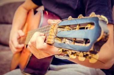 Adam yakın planda kahverengi gitar çalıyor.