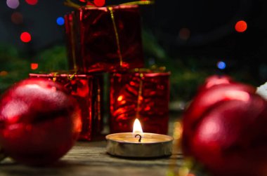 Ahşap bir masada yanan mum. Küçük hediyelerin ve ışık çelenklerinin arkasındaki Noel topları arasında. Güzel, sihirli Noel arkaplanı