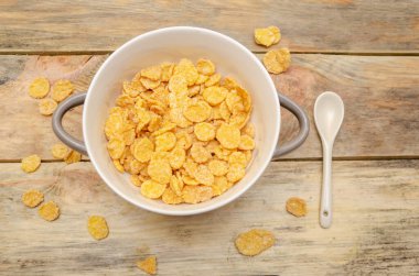 Tahta arka planda beyaz kaşıkla bir kase mısır gevreği.