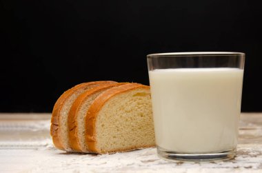 Bir bardak süt ve ahşap zemin üzerinde dilimlenmiş üç dilim ekmek. Siyah arka planda da un ve fotokopi alanı var.