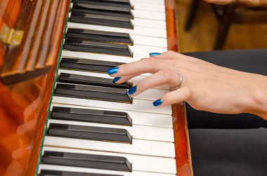 Mavi tırnak cilası olan genç bir kadının eli piyano çalıyor.
